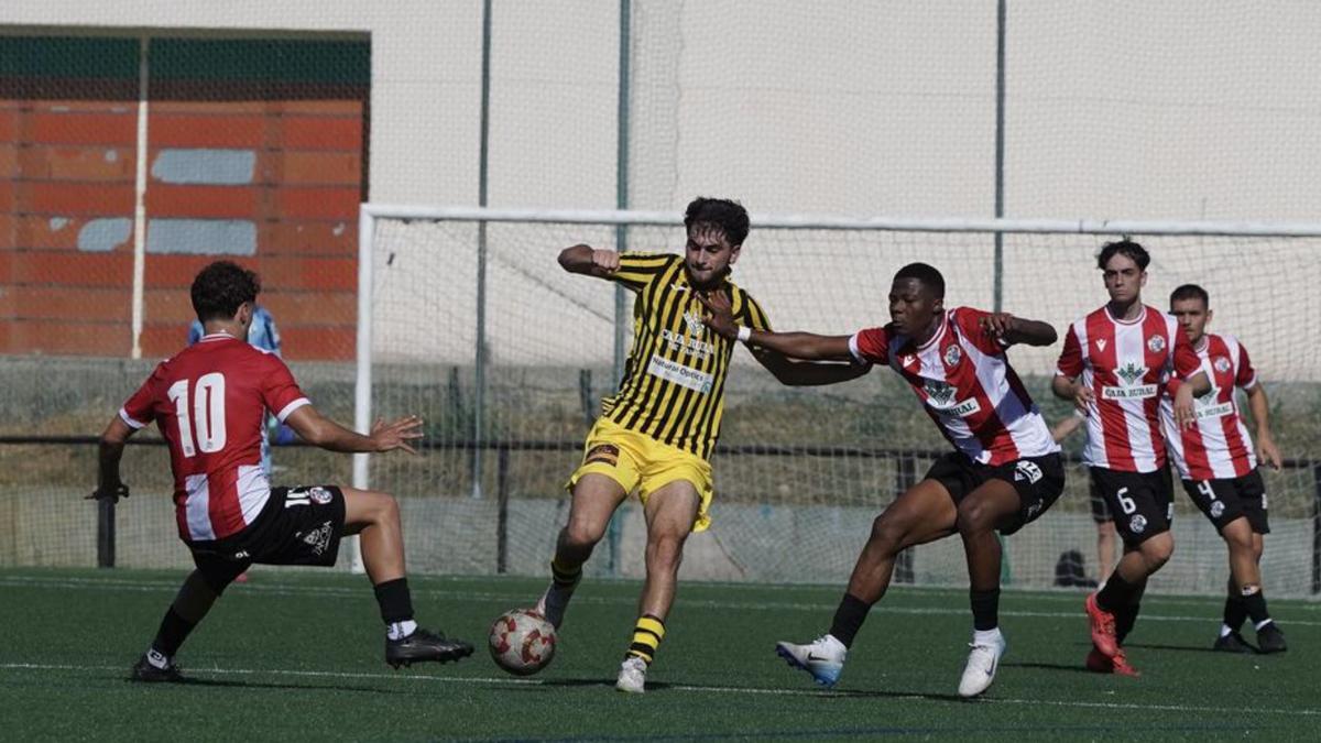 Un jugador del Moraleja CF golpea el balón entre dos futbolistas del filial. | JOSE LUIS FERNÁNDEZ
