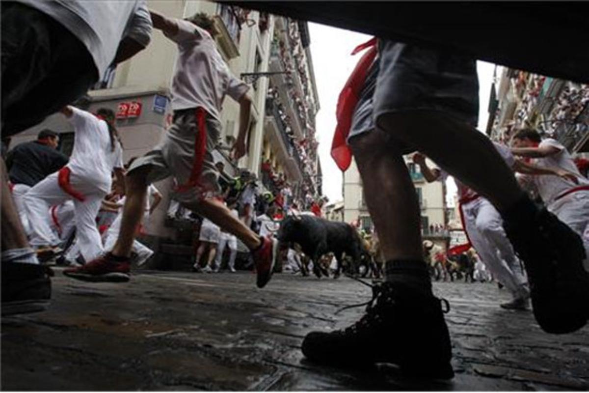 Pamplonesos i turistes corren al costat dels toros durant el primer ’encierro’ de les festes de Sant Fermí.