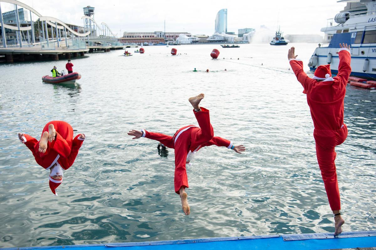 Tres nadadores disfrazados de Papá Noel se lanzan al agua para participar en la Copa Nadal en Barcelona, este viernes por la mañana.