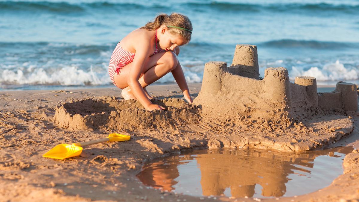 Una niña hace un castillo de arena en la playa