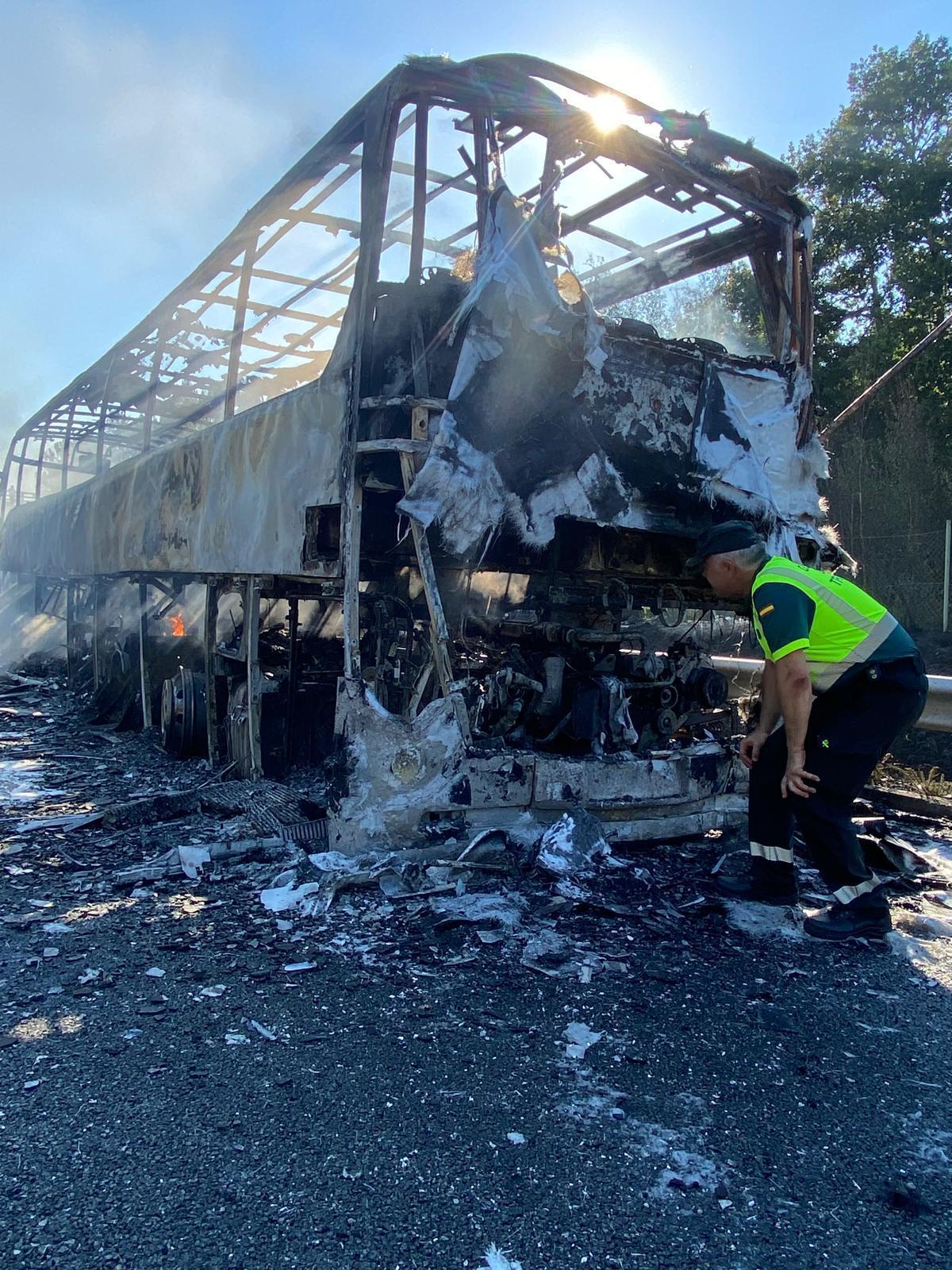 Un agente de la Guardia Civil de Tráfico examina el autobús, totalmente destruido por el fuego.