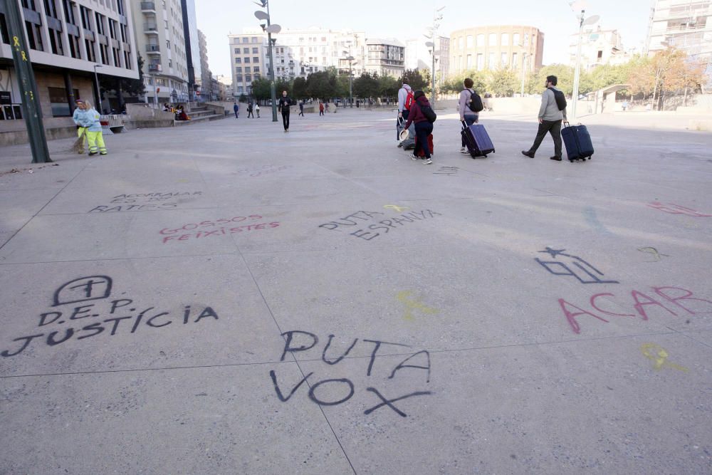 Carrers amb restes de mobiliari urbà cremat, contenidors per terra i treballadors de la brigada treballant