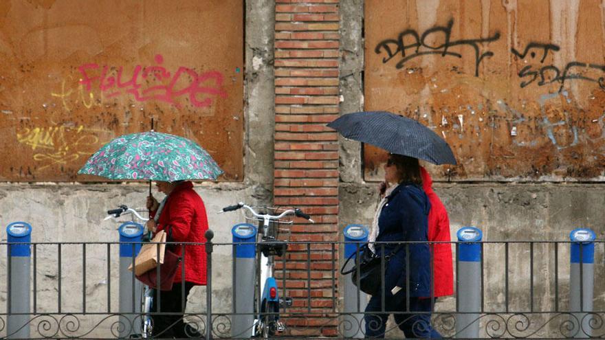 Varias personas pasean bajo la lluvia en la plaza de la Merced.