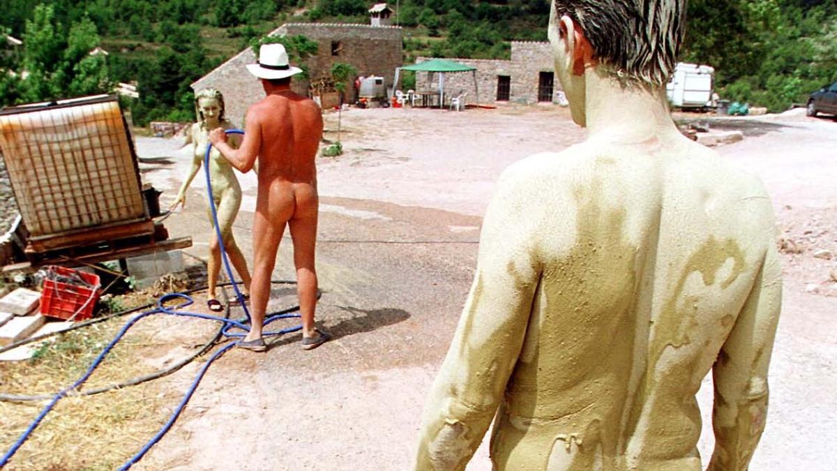 Unos naturistas toman un baño de arcilla y se lo quitan con una manguera en el pueblo naturista de El Fonoll.