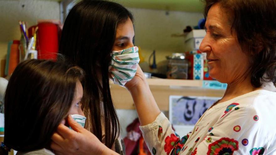 Una mujer coloca una mascarilla a dos niñas