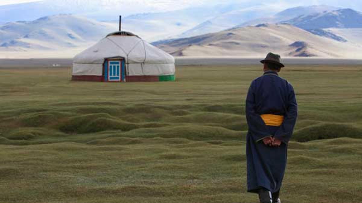Hombre mongol vestido con la indumentaria tradicional camina hacia una yurta.