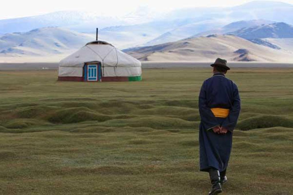 Hombre mongol vestido con la indumentaria tradicional camina hacia una yurta.