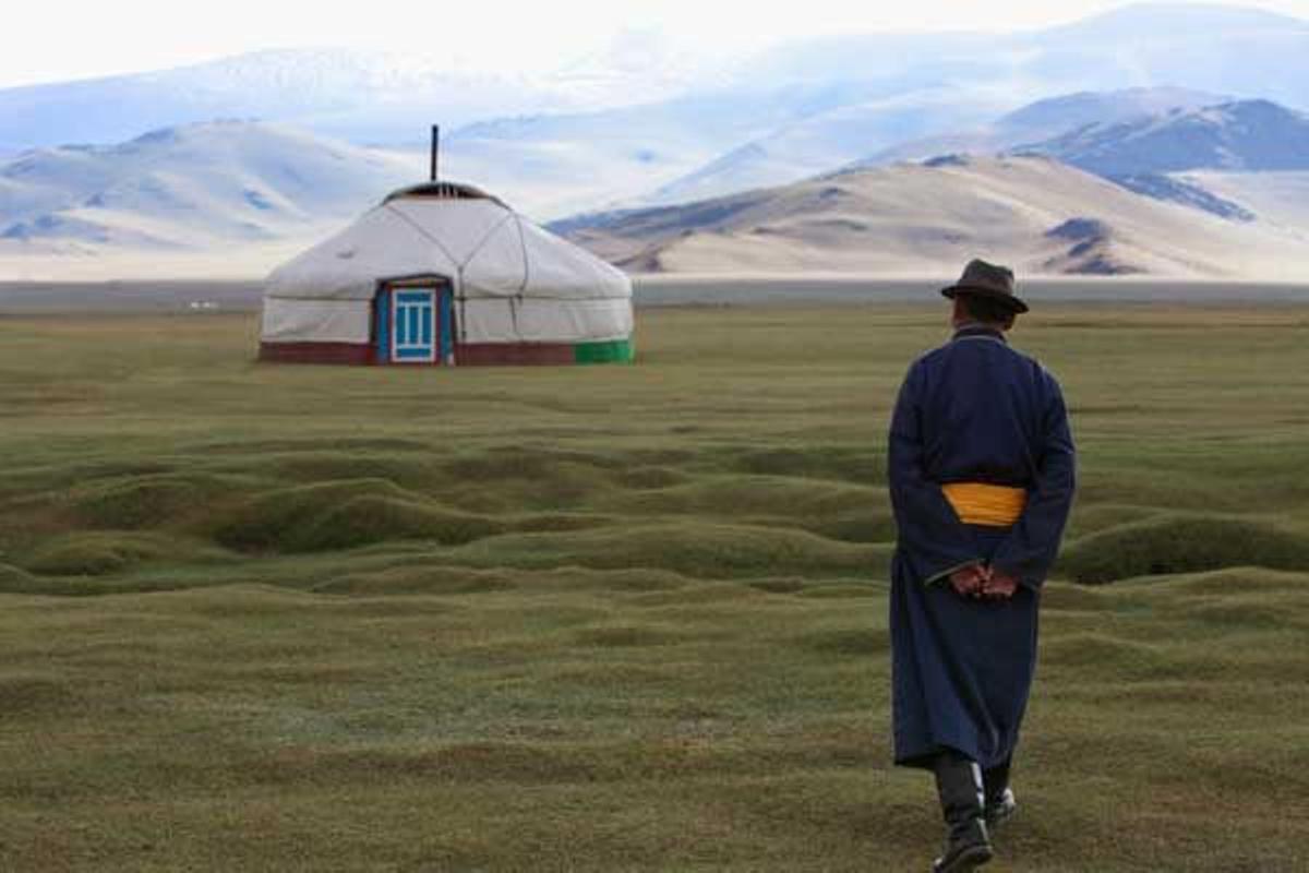 Hombre mongol vestido con la indumentaria tradicional camina hacia una yurta.