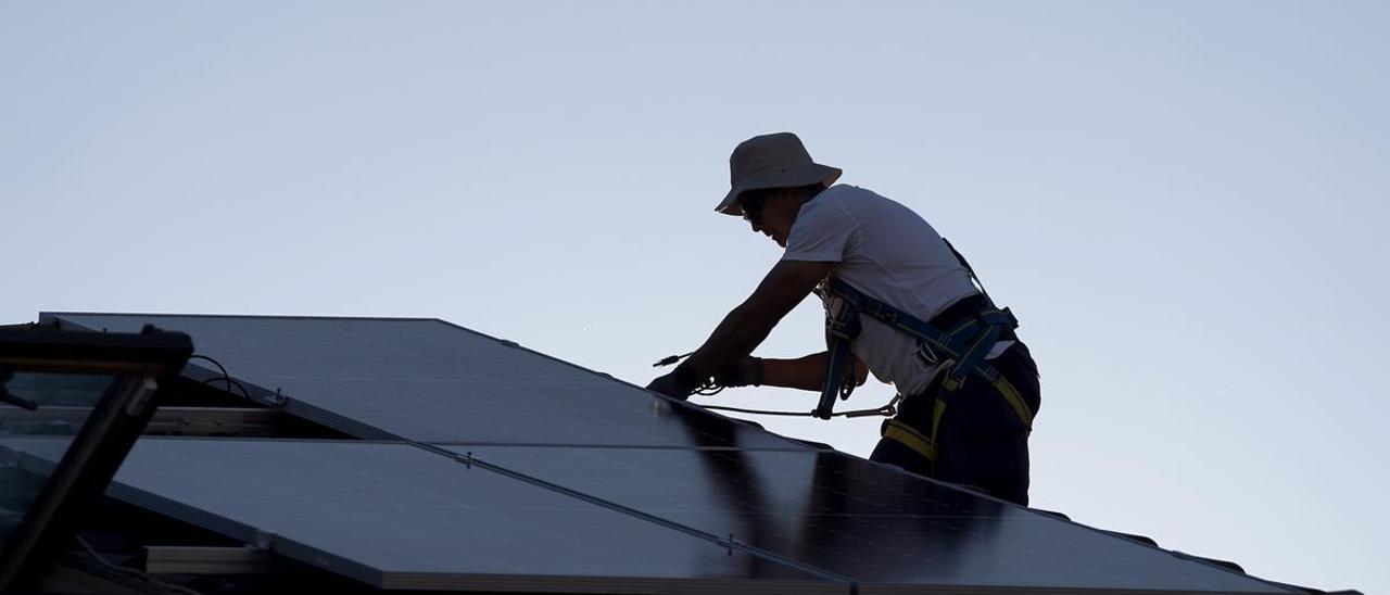 Un operario coloca paneles solares en el tejado de una vivienda unifamiliar.