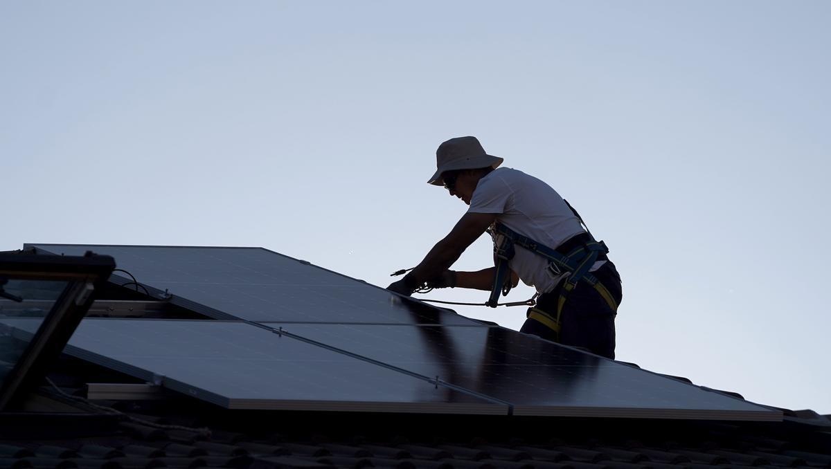 Un operario coloca paneles solares en el tejado de una vivienda unifamiliar. Un operario coloca paneles solares en el tejado de una vivienda unifamiliar.