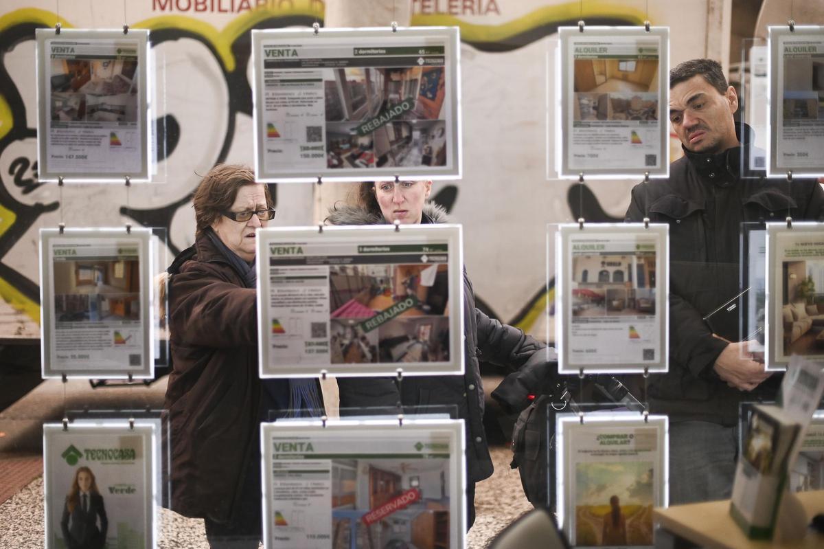 Tres personas miran los anuncios de alquiler en un escaparate.