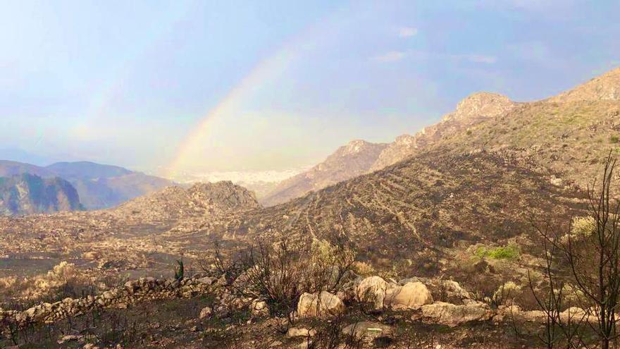 El arcoíris se ha dibujado en un cielo límpido y contrasta con el negro de las montañas calcinadas