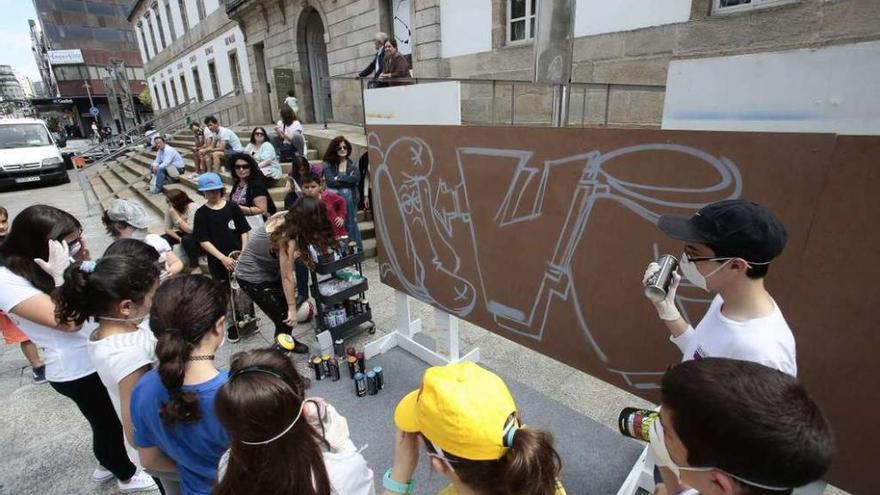 La artista Paula Blanco ayuda a los niños a pintar un grafiti frente al MARCO. // A. Irago