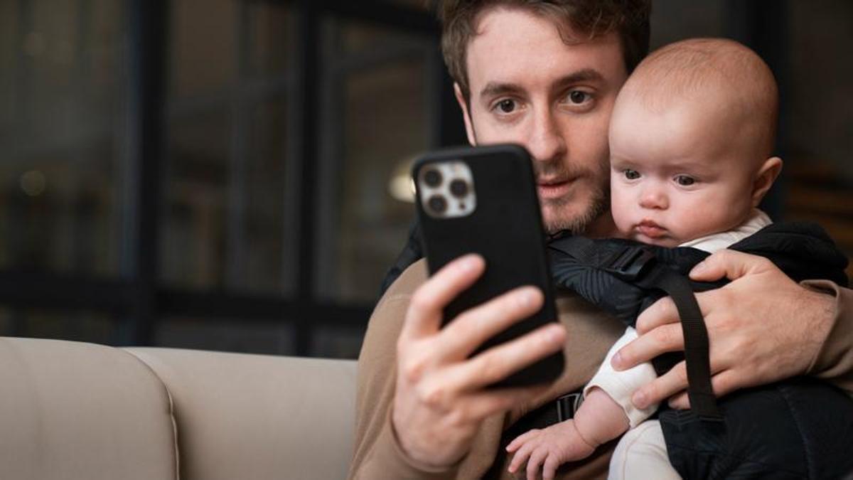 Un padre mira el móvil mientras que está con su bebé