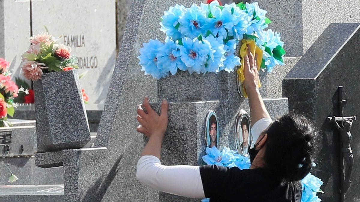 Una mujer limpia una lápida en un cementerio de La Almudena.