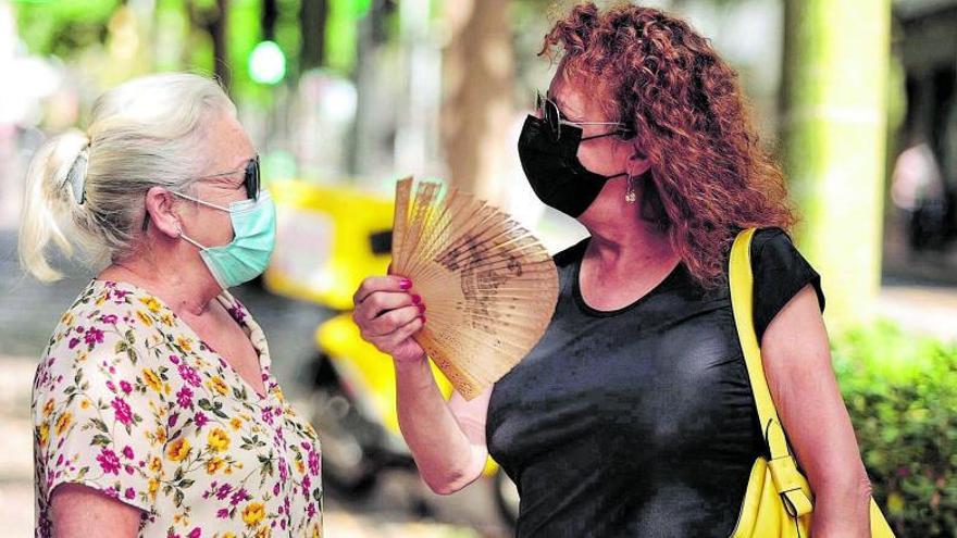 Dos mujeres se hablan en la calle, una de ellas con un abanico, durante la mañana de ayer.