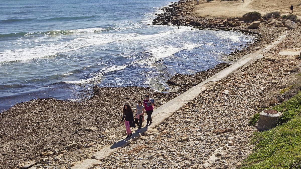 Jóvenes paseando ayer por encima del colector que ha quedado al descubierto por los embates del mar sobre esta zona de la playa.  