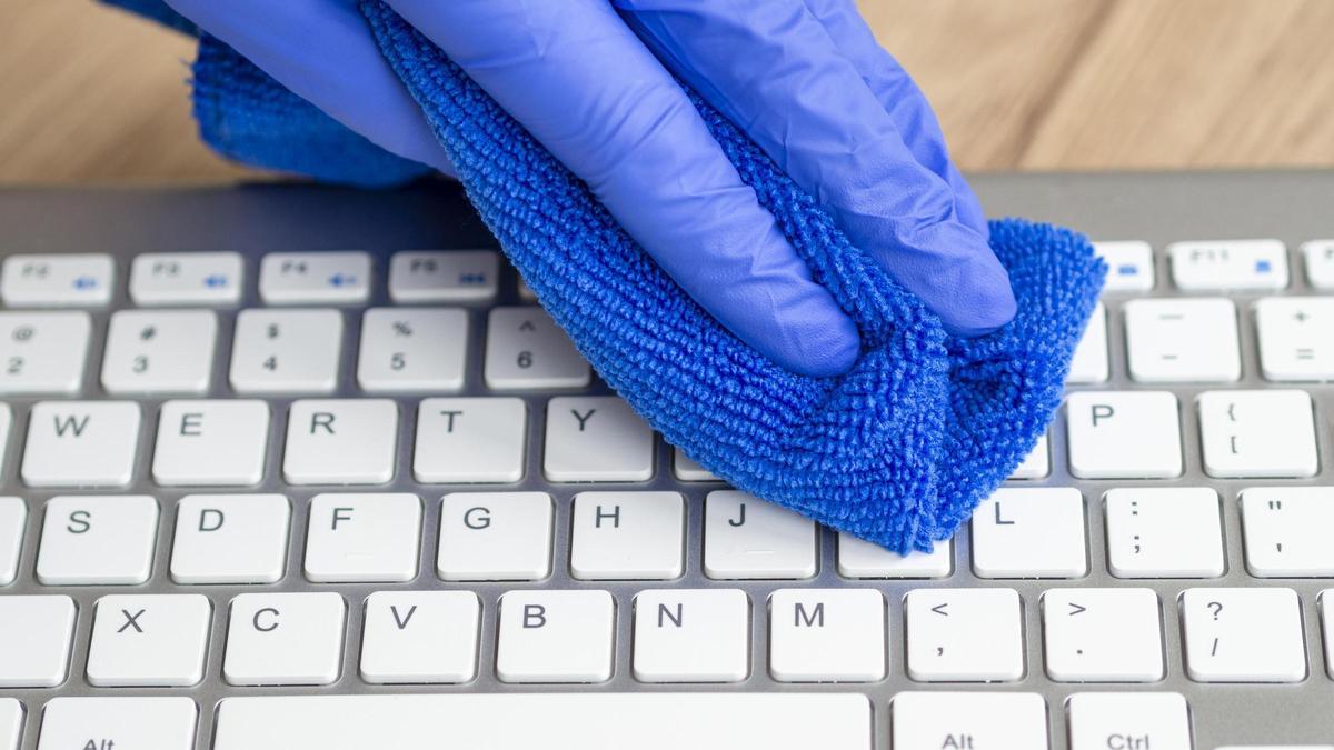 mano con guante quirurgico teclado de limpieza con pano