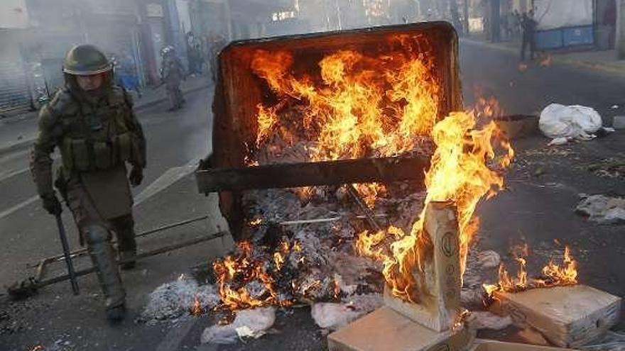 Un policía antidisturbios, junto a un contenedor incendiado. // Dpa