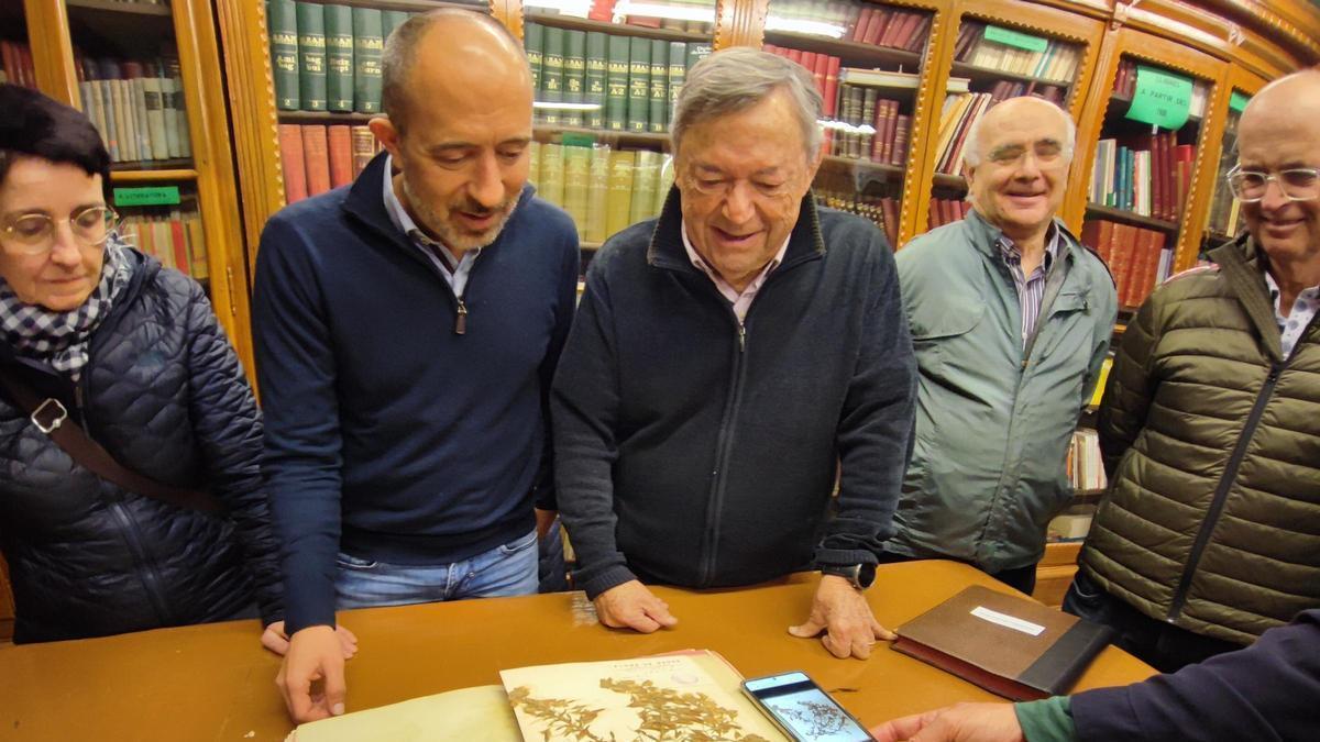 Aloy i Serra contemplen una pàgina de l'herbari, amb la versió digital en un telèfon mòbil al costat