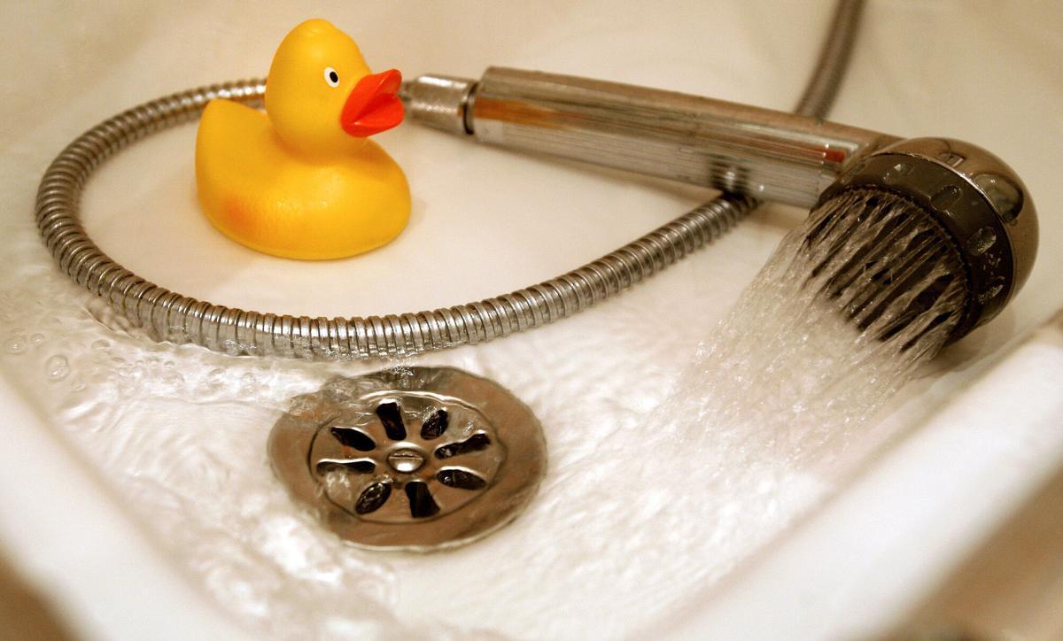 Una manguera de ducha y un patito de goma en el suelo de un plato de ducha.