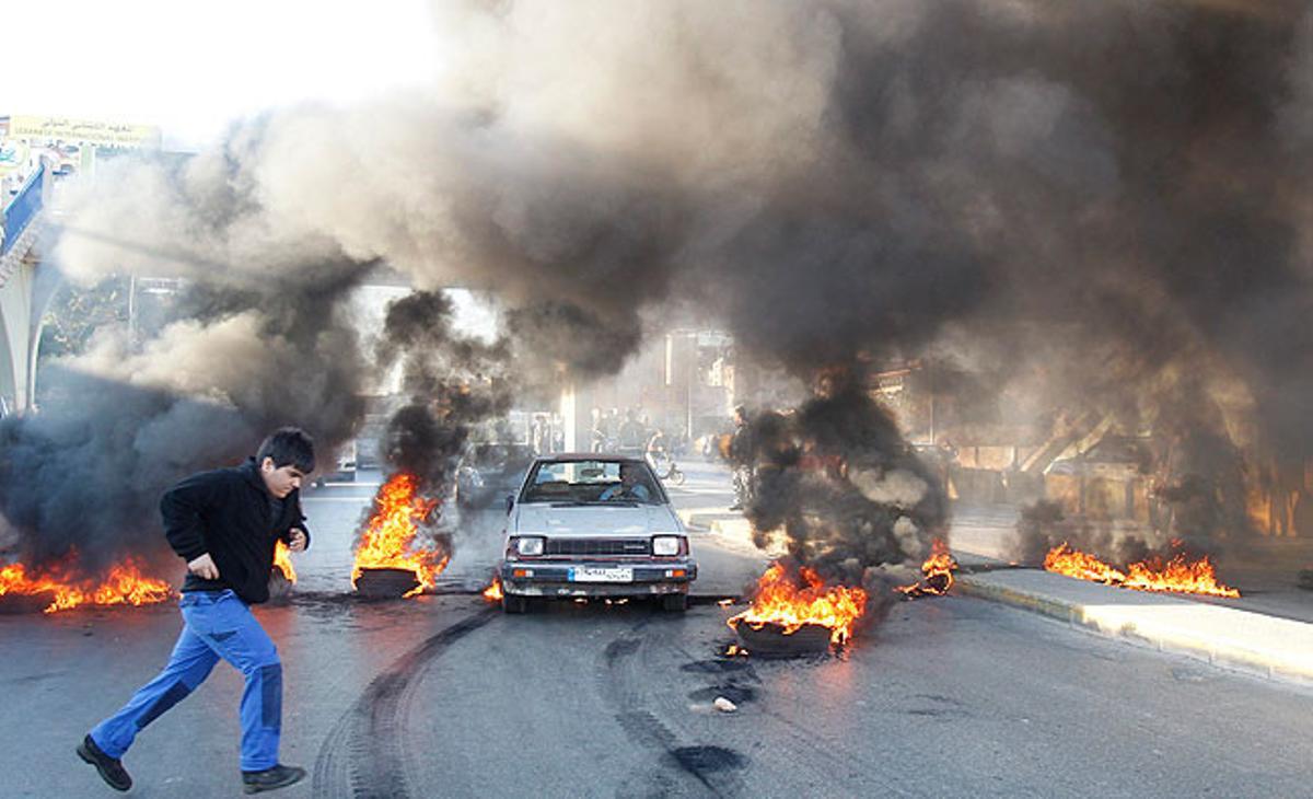 Un noi travessa el carrer mentre un cotxe intenta esquivar una barricada amb pneumàtics encesos, a prop de la presó de Roumieh, en una carretera que porta a Beirut.