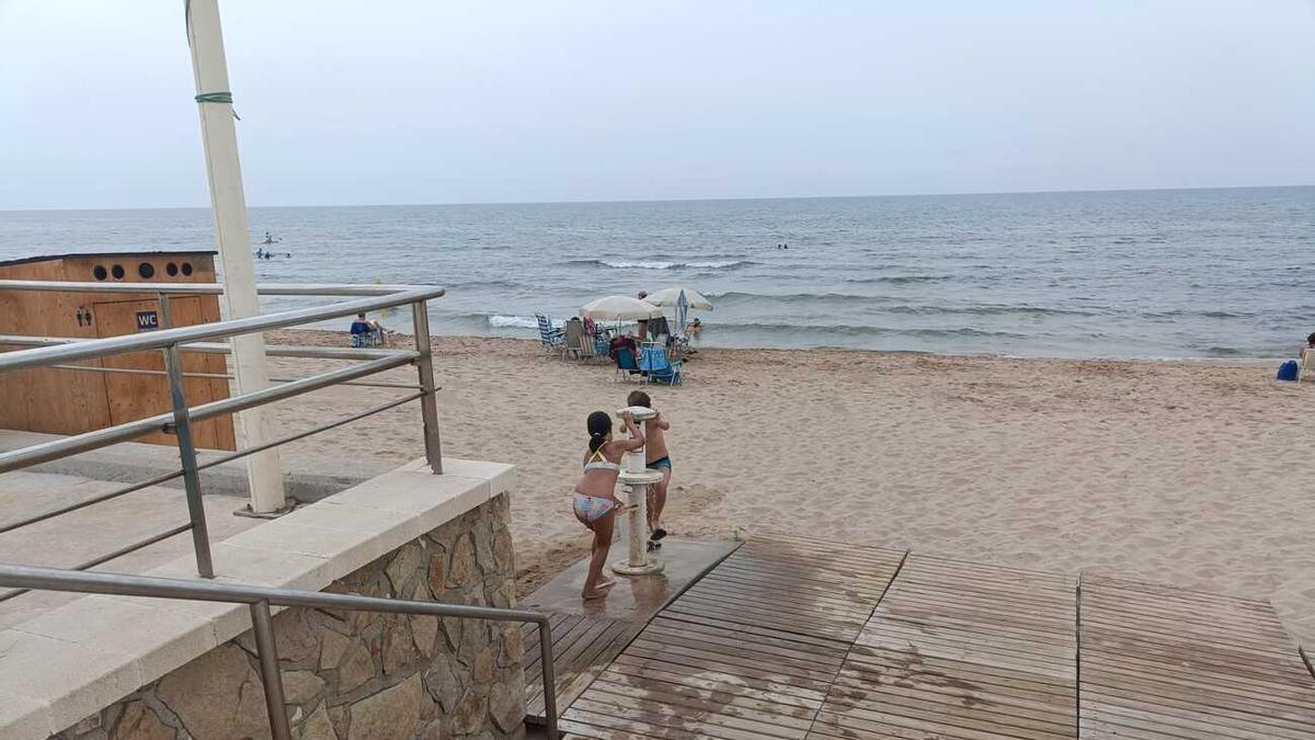 Unos niños se limpian en un lavapiés de la zona sur de la playa de Piles, en una imagen de este lunes.
