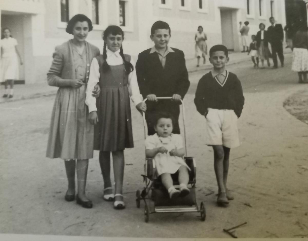 Isaura, conocida por sus allegados como Tita, es la pequeña de dos años, sentada en la silla y acompañada de sus tres hermanos y una vecina, en el cruce de la actual calle Aragón con Travesía de Vigo. (1956).