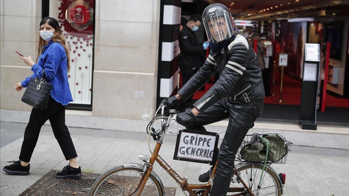 Un hombre monta su bicicleta con un cartel que dice gripe general, en la avenida Champs Elysee.