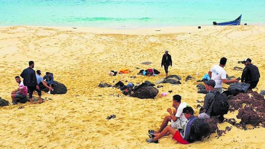 Un grupo de migrantes, a la derecha de la imagen, aguarda en la Playa de Las Conchas tras desembarcar de una patera ayer martes en La Graciosa. | | ALICIA PÁEZ 