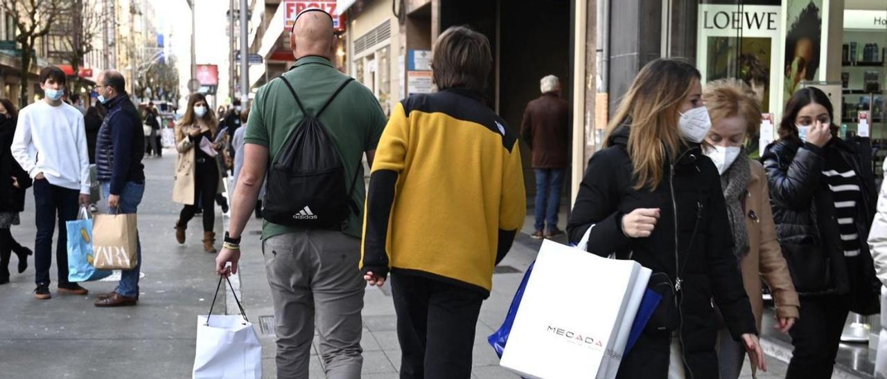 Arriba, dos clientas salen de un comercio en rebajas. Abajo, gente con bolsas en la “milla de oro” de Benito Corbal.   | RAFA VÁZQUEZ