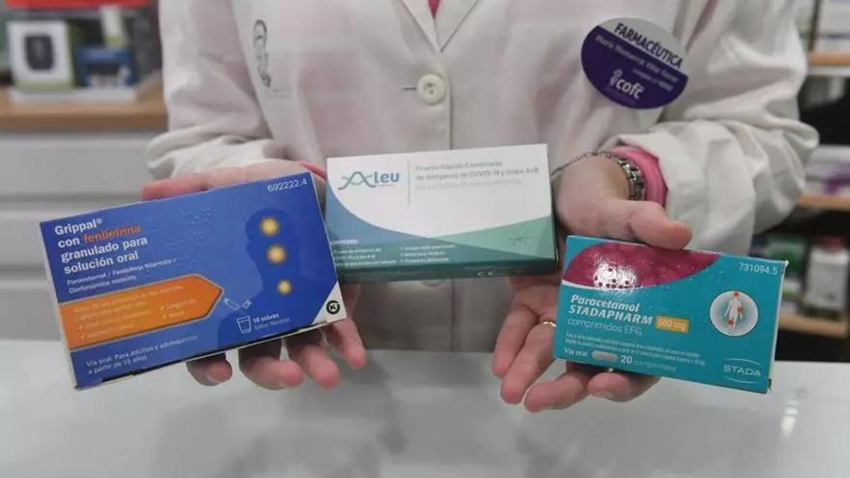 Una profesional de una oficina de farmacia muestra tres envases de diferentes medicamentos antigripales, en A Coruña.