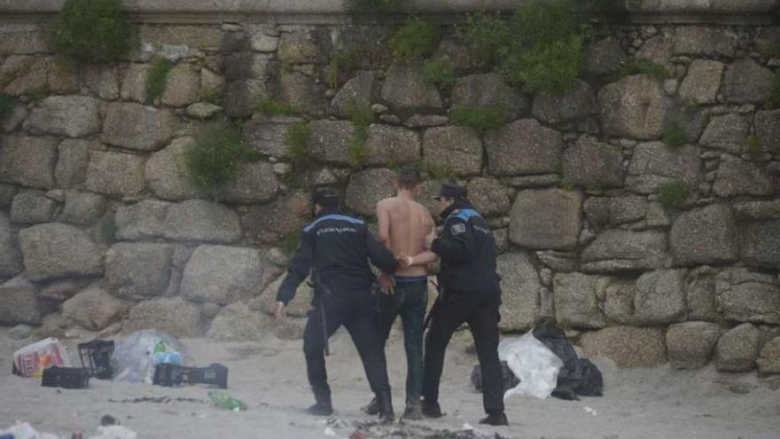 El joven que se bañó en el Orzán es conducido esposado por agentes municipales tras salir del agua.