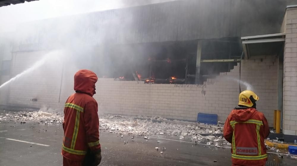 Los bomberos refrescan las paredes exteriores de la panificadora de Mercadona que el jueves quedó arrasada por el fuego.