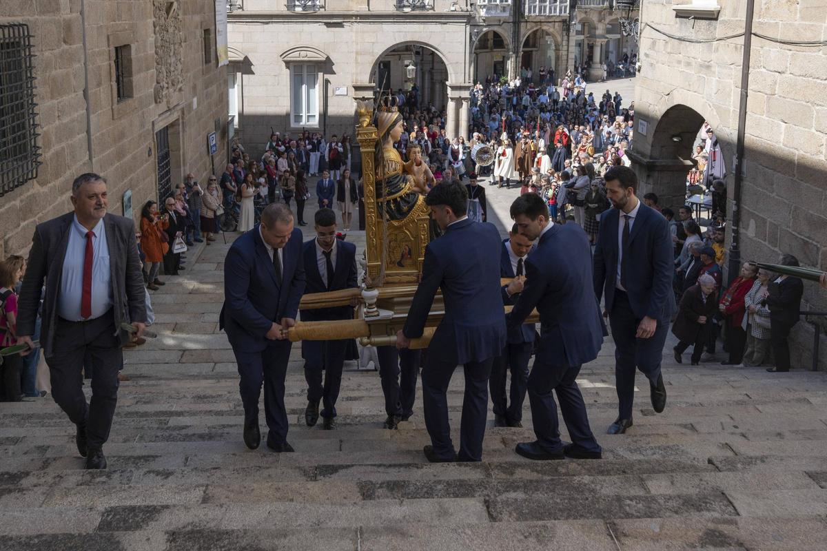 Un grupo traslada la imagen de Santa María Nai por la escalinata de acceso al templo, mientras al fondo esperan los concejales.