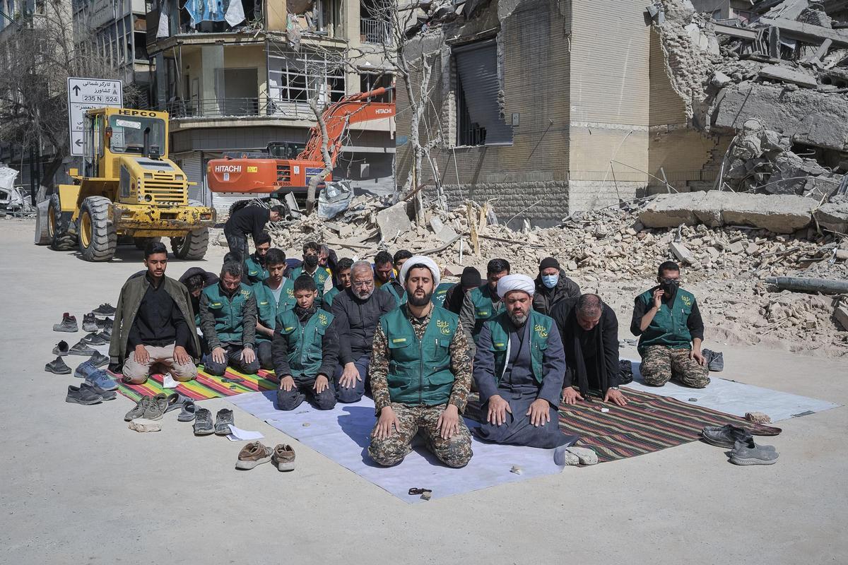 Un grupo de voluntarios basijis -milicia islámica- reza este miércoles, al lado de un edificio destruido en los bombardeos israelíes-estadounidenses contra Irán en la calle en la calle Kargar, cerca de la plaza Engelab en Teherán