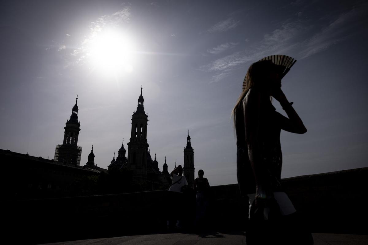 Una mujer protegiéndose del sol con un abanico mientras cruza el Puente de Piedra (Zaragoza)