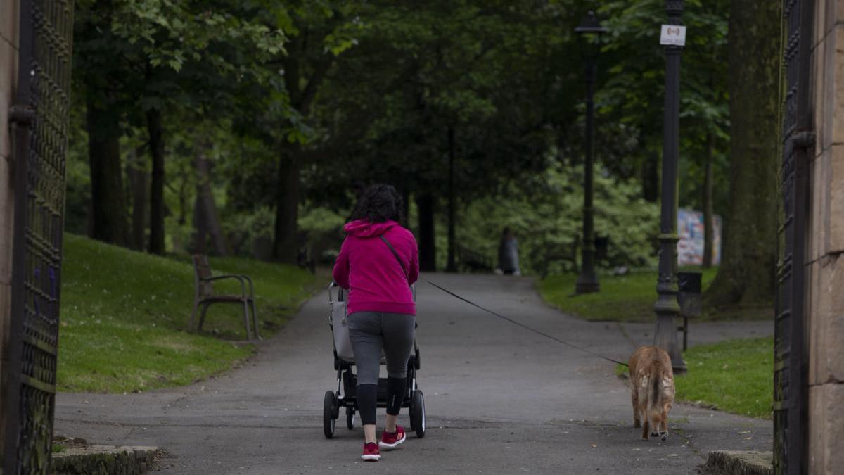 Una mujer pasea por un parque y lleva a su perro atado con una correa