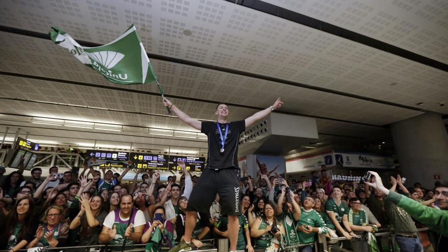 Alen Omic, subido en una valla en el hall del la terminal de llegadas del aeropuerto de Málaga, arenga a la afición con una enorme bandera cajista.