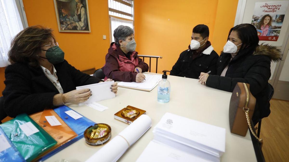 Por la izquierda, Mabel Menéndez, responsable de acogida en Cáritas Piedras Blancas, y Martina Sampedro, la directora, atienden a Carlos Javier Álvarez y Norma Belisario de Álvarez. | Luisma Murias