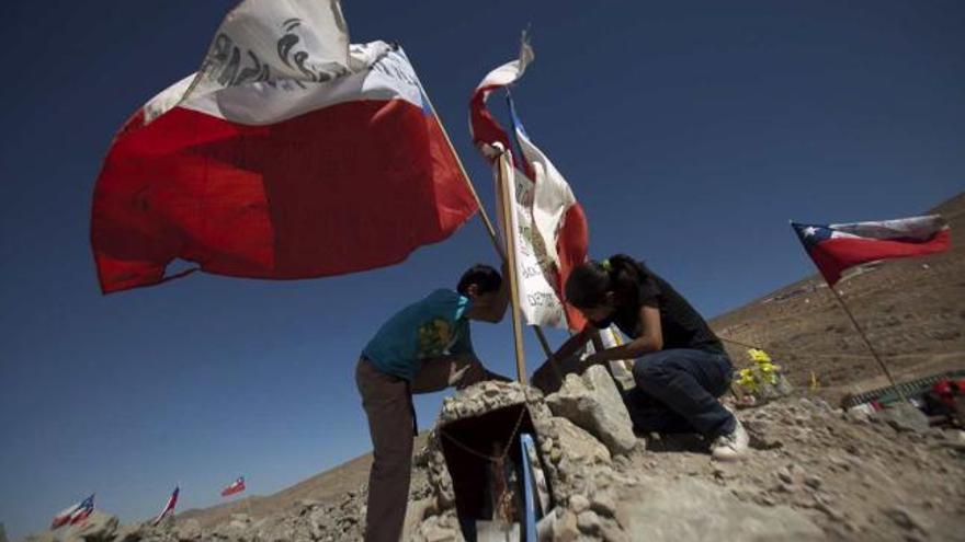 Dos niños colocan una bandera chilena en el yacimiento donde se encuentran los mineros.