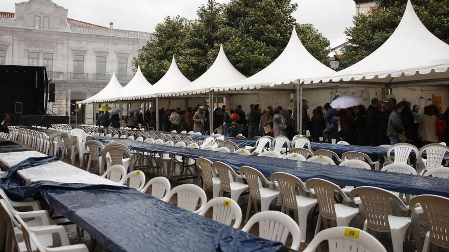 Asistentes a la paella solidaria en el Antiguo, protegidos de la lluvia bajo una de las carpas, con las mesas vacías. | MARIO CANTELI