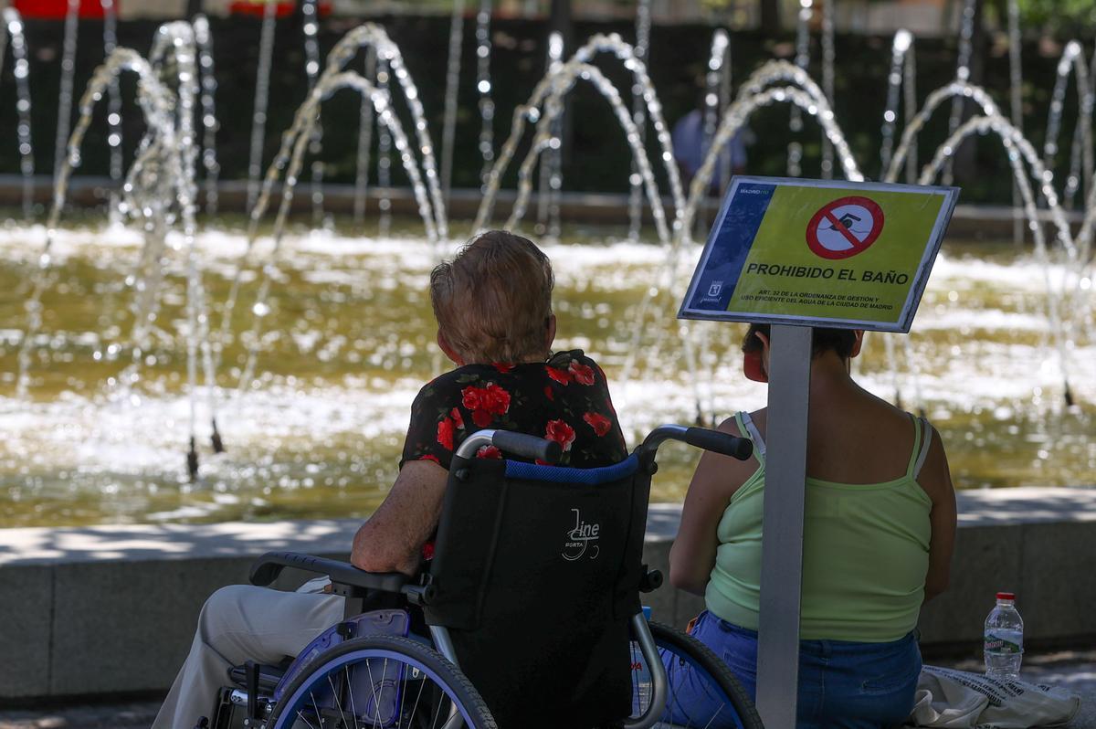 Niños y adultos se refrescan a la sombra, junto a las fuentes públicas del parque del Retiro, en Madrid.