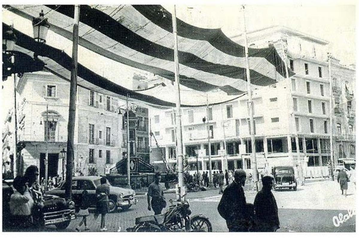 Imagen de los años sesenta, con vehículos y el edificio que se negó a acoger los anclajes en plena construcción