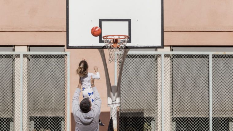 Un padre y su hija juegan a baloncesto en el patio de una escuela