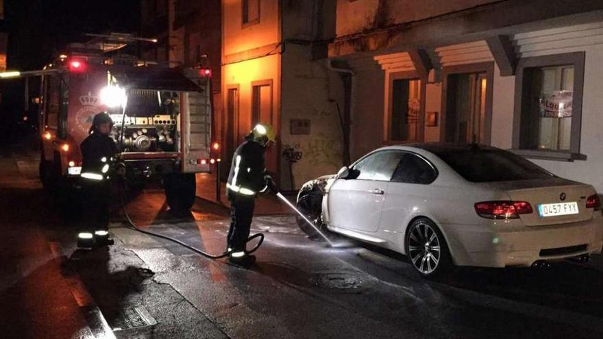 Los bomberos ante el vehículo incendiado a la altura de una rueda. // Muñiz