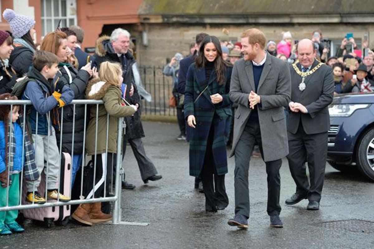 Meghan Markle con abrigo estampado de Burberry, pantalones negros y bolso verde junto al príncipe Harry