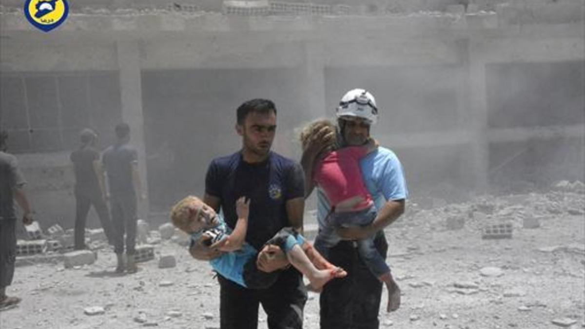 Voluntarios de la Defensa Civil con niños, tras un bombardeo en Daraa.