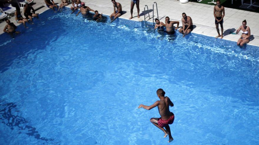 Un joven a punto de introducirse en el agua tras saltar desde la plataforma de salida de una piscina.