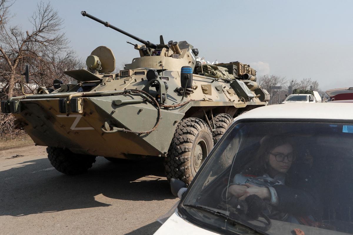 Una refugiada espera en su coche mientras un vehículo de tropas prorrusas sale de un control en los alrededores de Mariúpol, el 24 de marzo.